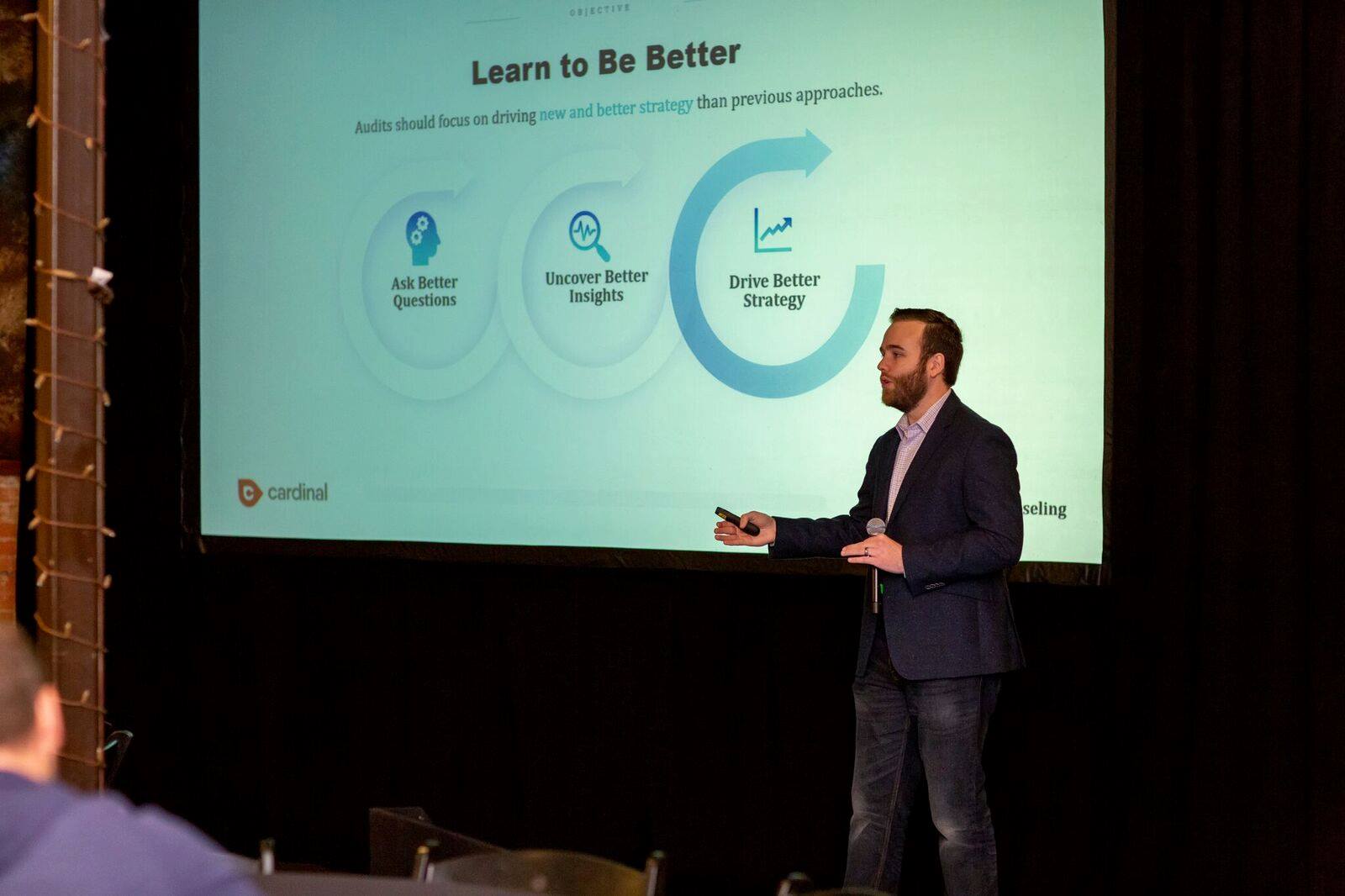 John McAlpin presenting on stage at State of Search Conference with presentation slides visible behind him